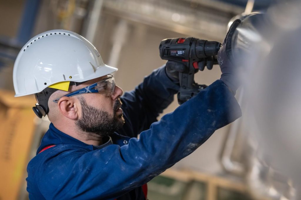 Man met boormachine en veiligheidsuitrusting aan het werk.