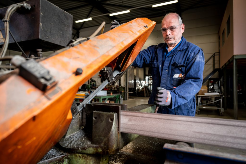Man bedient industriële zaagmachine in werkplaats.