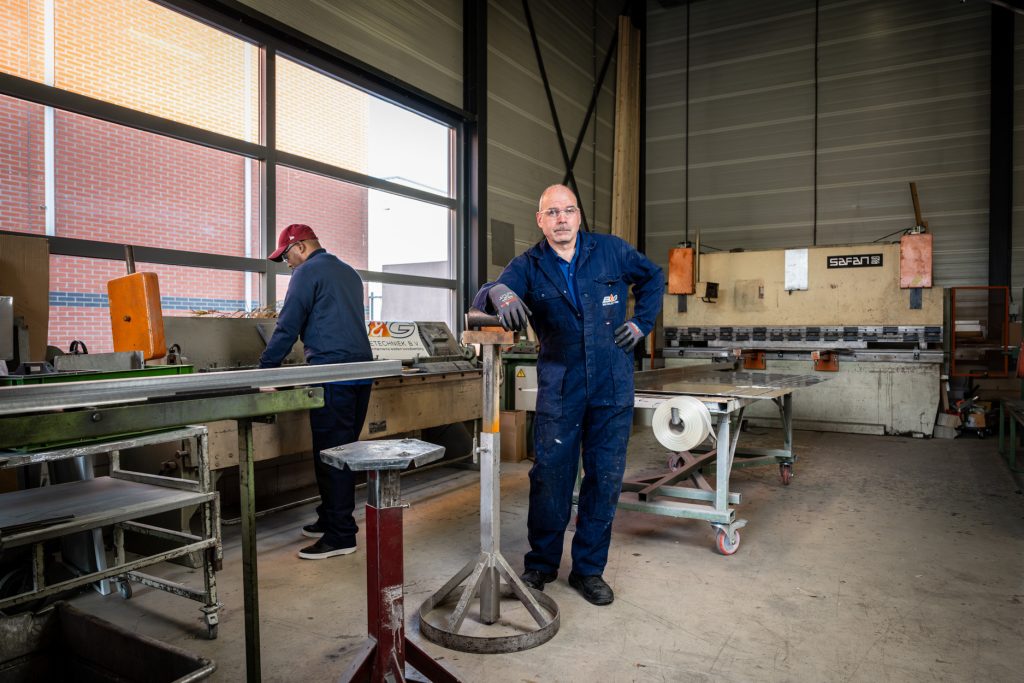 Twee werkmannen in een fabriekshal met machines.