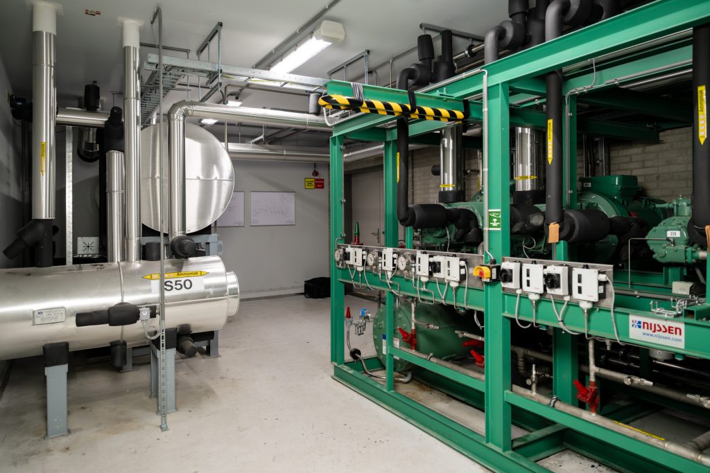 Industrieel machinekamerinterieur met groene pijpleidingen en apparatuur.